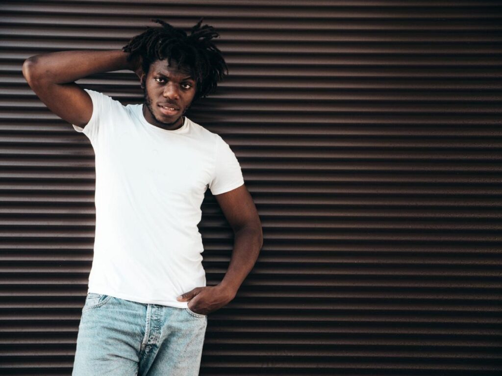portrait-handsome-hipster-modelunshaven-african-man-dressed-white-summer-tshirt-jeans-fashion-male-with-dreadlocks-hairstyle-posing-near-roller-shutter-wall-street