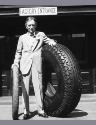 Harvey Firestone Sr. standing at the Akron, Ohio, factory entrance with an original Firestone non-skid tread tire and a large tire, ca. 1926-1930 (Image Courtesy: PRNewswire)